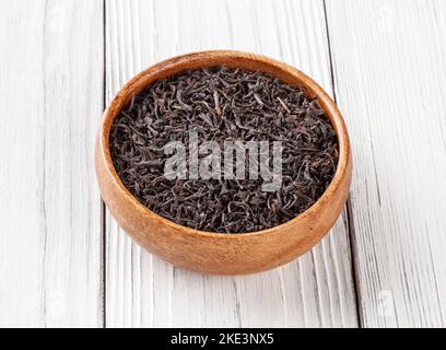 Dry black tea in wooden bowl on white wooden background Stock Photo
