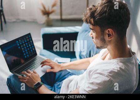 Side view of a man in white T-shirt with collagen patches under the eyes looking into laptop screen. Skincare concept. Cosmetology concept. Daily Stock Photo