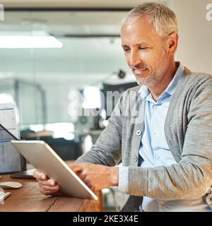 Business at a touch. a mature businessman using a digital tablet while sitting at his desk in his office. Stock Photo