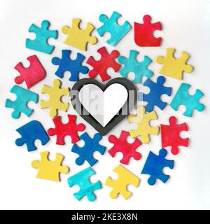 Autism campaign symbols. Colorful puzzle pieces around blackboard stone heart with copy-space. Flat lay, top view, square composition on off white Stock Photo