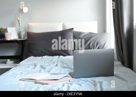 Laptop computer and notebooks on bed with soft light from window Stock Photo