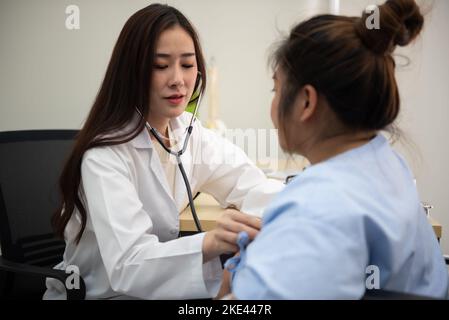 Asian female doctor cardiologist examining fat woman cardiac patient listening checking heartbeat using stethoscope. Stock Photo
