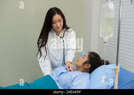 Smiling Asian female doctor using stethoscope listening checking heartbeat fat woman patient on the bed, examination and diagnosis. Stock Photo