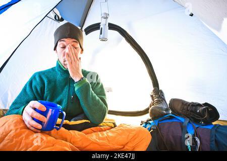 Young man early in the morning waking up in his tent on a backpacking trip. Stock Photo