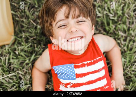 An overhead shot of a smiling child laying on a green grass field Stock Photo