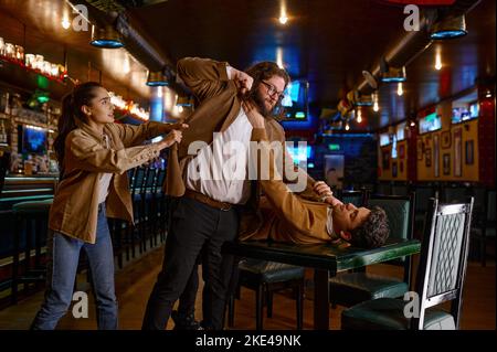 Young woman trying to separate craze mad fighting friends Stock Photo