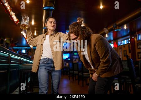 Fury woman with beer glass attacks man, conflict at sport bar Stock Photo