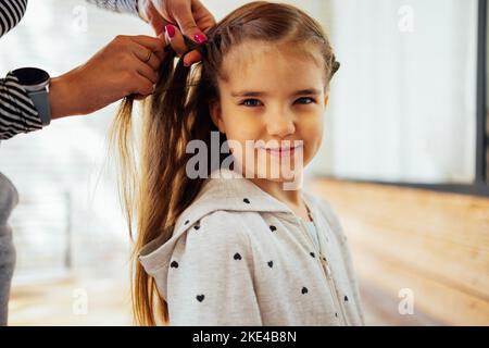 Hairdresser is braiding the hair of the girl. Getting ready for school Stock Photo