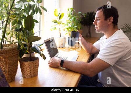 Young personal development coach answering the client by email by a laptop while having break in a coffee shop. Hipster guy searching the information Stock Photo