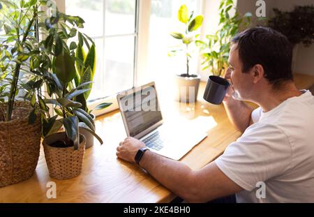 Young personal development coach answering the client by email by a laptop while having break in a coffee shop. Hipster guy searching the information Stock Photo