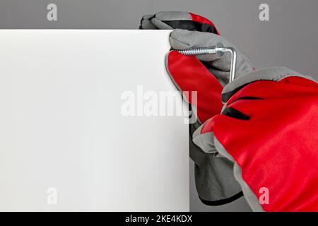 Furniture assembler in red gloves is screwing in a screw with a Stock Photo