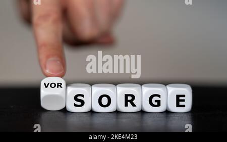 Hand turns dice and changes the German word 'Sorge' (concern) to 'Vorsorge' (precaution). Stock Photo