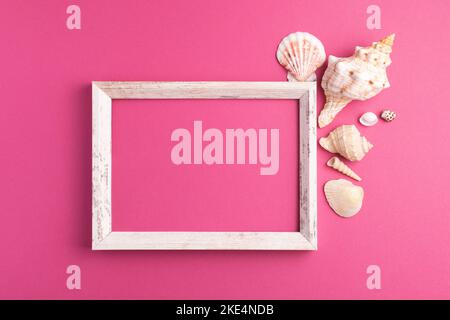 Top view of blank wooden picture frame with seashells decorations isolated on bright pink background. Mock up, copy space, flat lay. Stock Photo