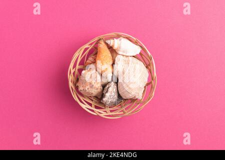 Top view of wicker basket with sea shells isolated on bright pink background. Stock Photo