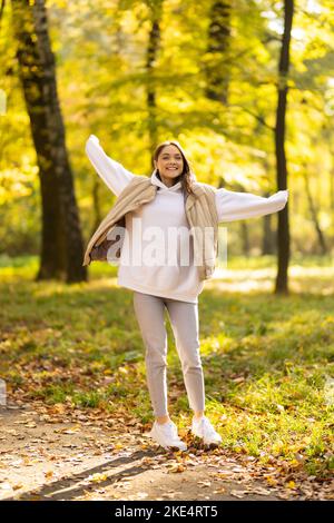 Hello november. smiling trendy woman in beige coat and orange hat rejoicing outside in the city park in autumn. Stock Photo