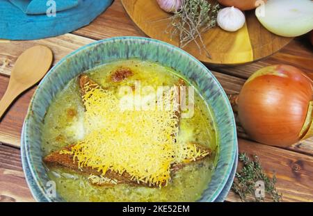 Closeup of isolated blue bowl with onion soup, gratinated toast bread and grated parmesan pecorino cheese, thyme, garlic, onions ingredients on wood t Stock Photo