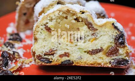 Close up of isolated sliced christstollen with raisins, white powdered sugar and marzipan on red plate Stock Photo