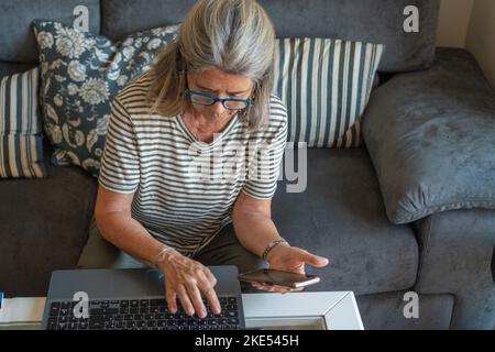 mature woman using cell phone and laptop at home Stock Photo