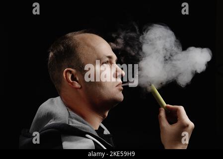 A man uses an electronic cigarette against a black background. Space for text. Alternative to smoking. How to quit smoking. Stock Photo