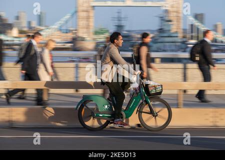 A man commuting on a HumanForest electric hire bicycle across London Bridge, during rush hour.  London Bridge, London, UK.  17 Oct 2022 Stock Photo