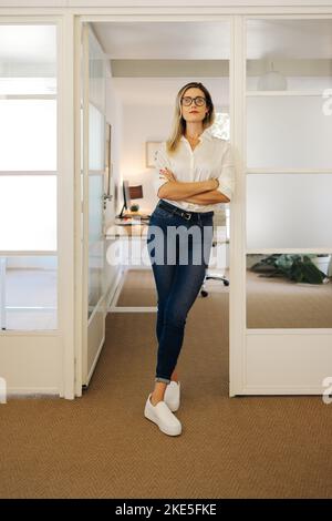 Confident young businesswoman looking at the camera while standing in front of her office. Successful businesswoman working in a creative workplace. Stock Photo