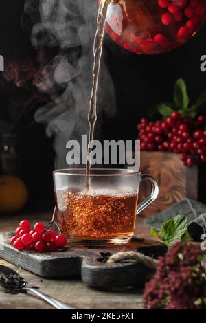 Viburnum tea is poured into a cup with steam, pouring process. Autumn ...