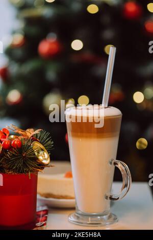 Vertical images of cup of milkshake with straw on white table against background decorated Christmas tree. Concept festive drinks and happy new year Stock Photo