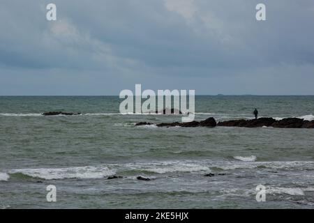 A fisherman observes the sea, the weather is bad. The sea is green and the sky blue gray. Stock Photo