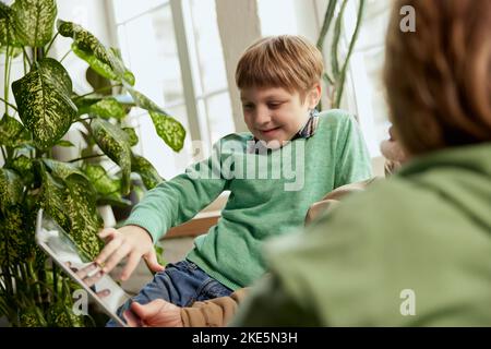 Old grandparents with grandchild sitting on couch at home and reading news, funny stories. Watching reels at laptop. Happy time in friendly and cozy Stock Photo