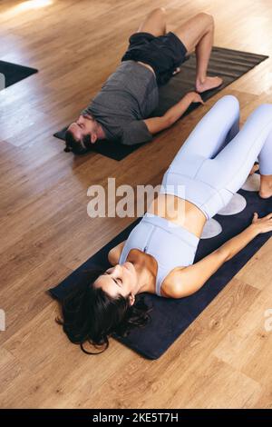 High angle view of young people doing the glute bridge exercise while lying on fitness mats in a yoga studio. Sporty man and woman practicing hatha yo Stock Photo