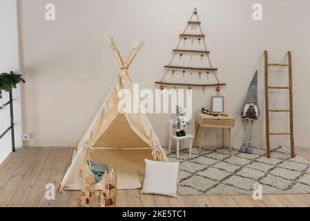 Christmas nursery in scandinavian style. Eco friendly interior, wooden toys, wigwam made of natural materials. On the wall is Christmas tree made of w Stock Photo