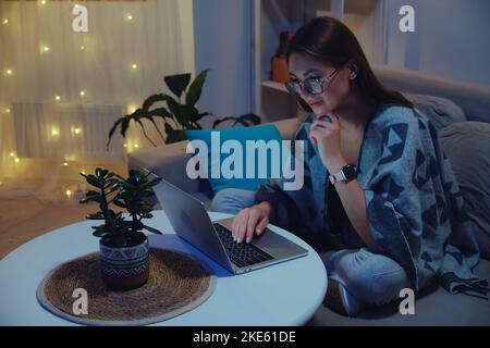Young smiling woman using laptop at night while working overtime against christmas lights background Stock Photo