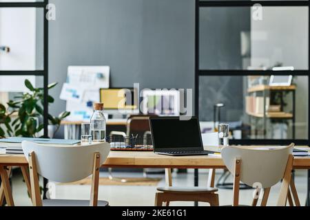 Workplace of modern creative designer or other employee with laptop standing on desk surrounded by chairs in coworking space Stock Photo