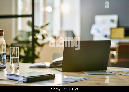 Laptop surrounded by business documents, notebook, bottle and glass of water and other supplies standing on workplace of manager Stock Photo