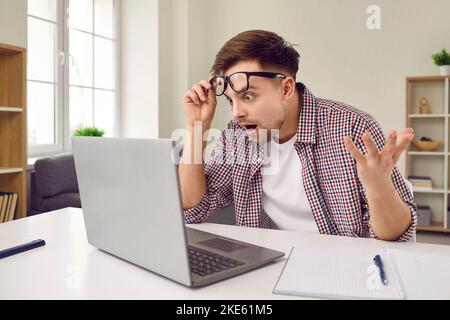 Young man looks at his laptop computer with surprised, shocked and happy face expression Stock Photo