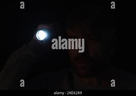 man with bright flashlight looking away in darkness isolated on black Stock Photo