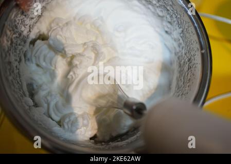 Extreme close up of a hand mixer mixing white egg cream in a bowl Stock Photo