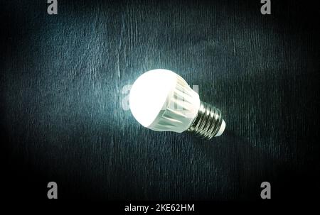 Luminous LED lamp on a dark wooden background. Energy saving technology. Stock Photo