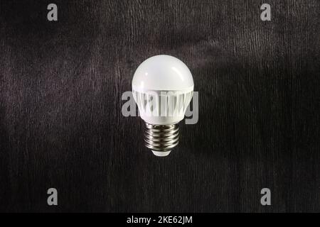 A LED lamp on a dark wooden background. Energy-saving technology. Stock Photo