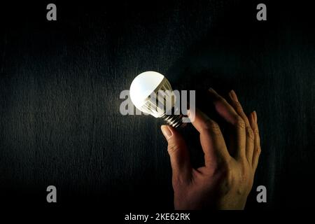 LED lamp on a dark wooden background in a woman's hand. Energy-saving technology. Stock Photo