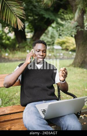 Young African man talking on phone disputing over computer, stressed, unsatisfied. Disappointed, confused, angry male arguing with technical online support or customer service. Bad connection concept Stock Photo