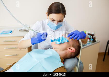 Male patient sits on the dentist's chair and receives teeth restoration, female dentist at the dental clinic. Selective focus Stock Photo