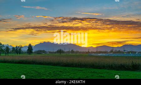 Sonnenuntergang im Rheintal, mit Wiesen und Felder, Bäumen und Schweizer Bergen im Hintergrund. Föhnwolken und blau, gelb, orange und rotem Himmel Stock Photo
