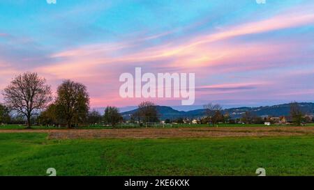 Sonnenuntergang im Rheintal, mit Wiesen und Felder, Bäumen und Schweizer Bergen im Hintergrund. Föhnwolken und blau, gelb, orange und rotem Himmel Stock Photo