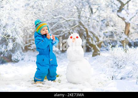 Children build snowman. Kids building snow man playing outdoors on sunny snowy winter day. Outdoor family fun on Christmas vacation. Stock Photo