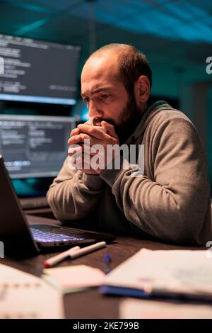Young man feeling cold and drinking cup of coffee, using hot beverage to get warm in office late at night. Male coder serving caffeine refreshment and programming new user interface. Stock Photo