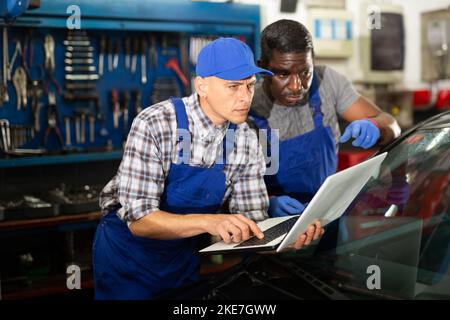 Two auto mechanics diagnosing car engine with laptop Stock Photo