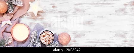 Cozy Christmas or winter corner border with grey and dusty pink sweater, candle, hot chocolate, snowy branches and decor. Overhead view on a rustic wh Stock Photo