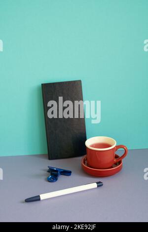 Notebook, pen, clip, cup of tea on purple desk. blue background. workspace Stock Photo