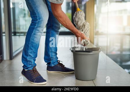 Using the perfect amount of water. an unrecognizable man ringing out a mop while cleaning the office floor. Stock Photo